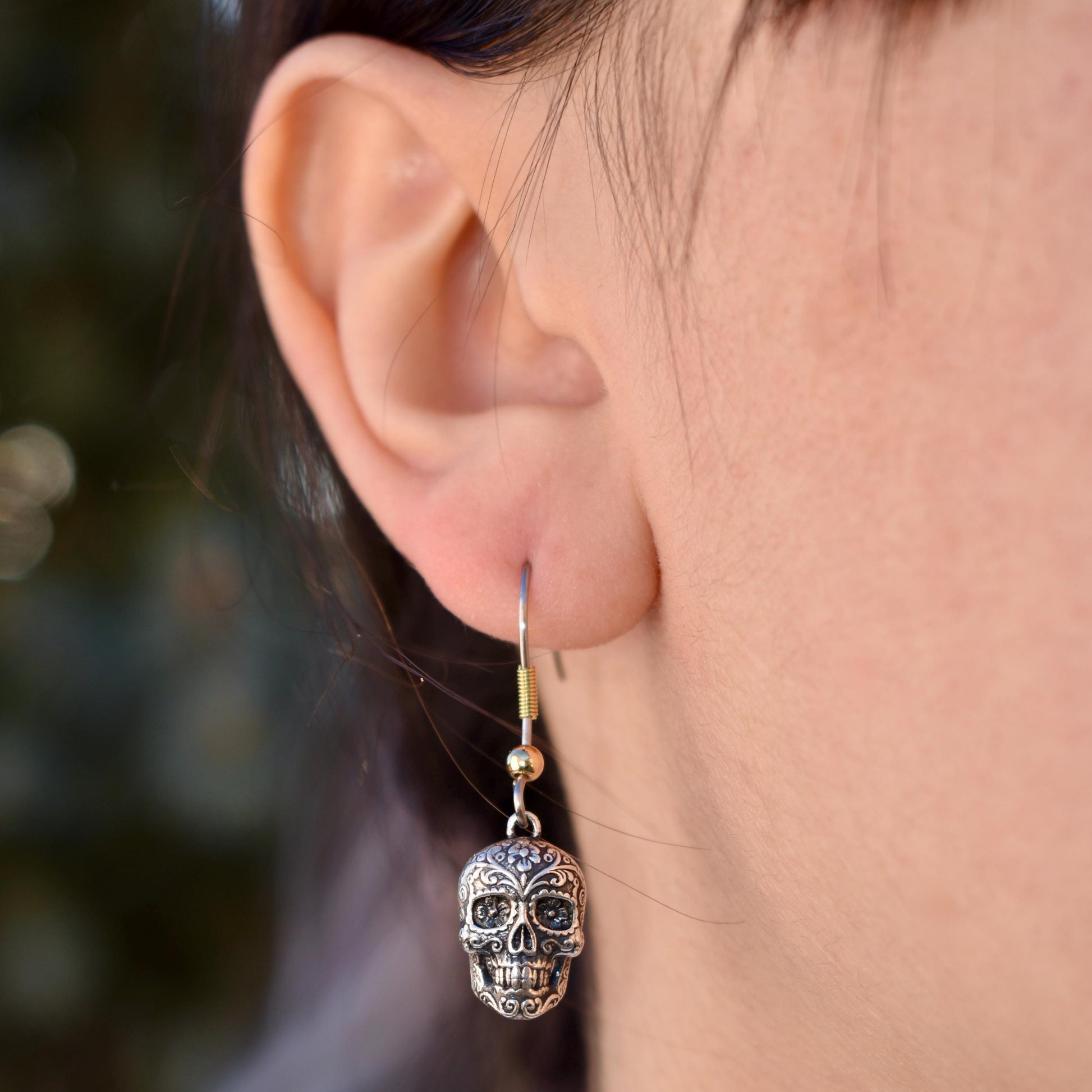 A Woman Wearing A Dia De Los Muertos Sugar Skull Charm As Earrings - Handcrafted .925 Sterling Silver Pendant for Bracelets and earrings by The Colorado Charm Company - Front view